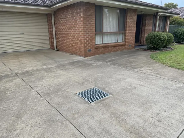 Concrete driveway with a metal drain grate beside a brick house and garage in Wakeley