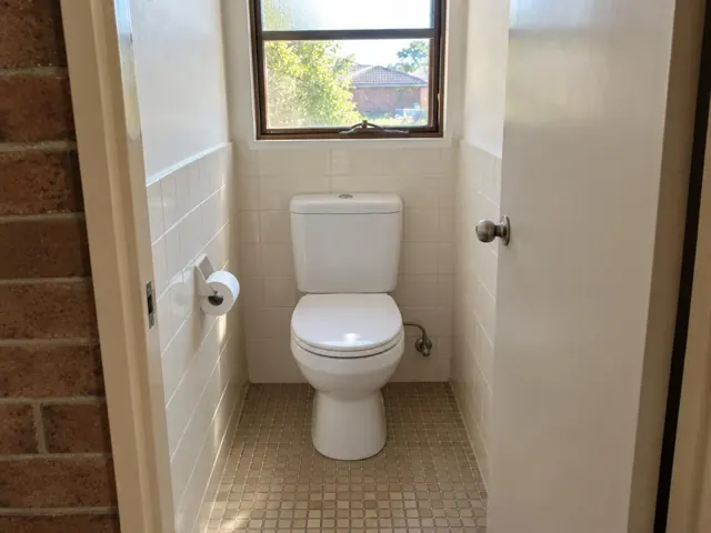 Clean toilet in a small tiled bathroom with a window and brick doorway in Bonnyrigg