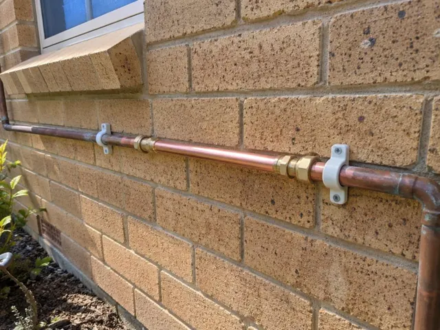Repaired copper water pipe on a brick exterior wall below a window in St Johns Park