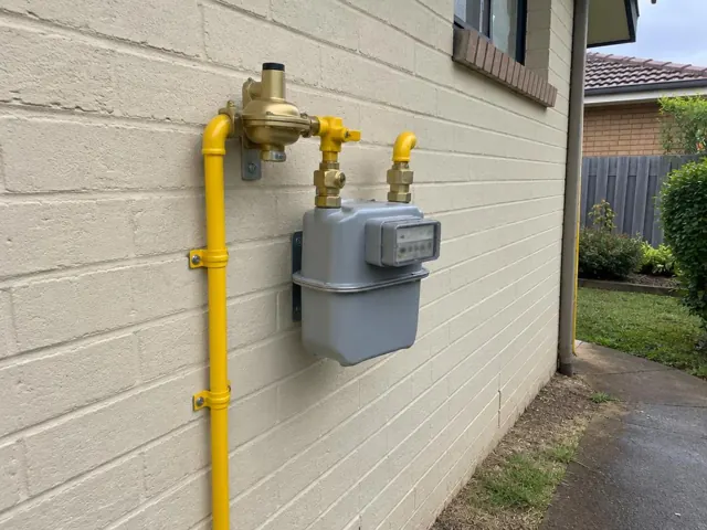 Outdoor gas meter with new yellow gas fittings on a brick wall beside a home in Canley Heights